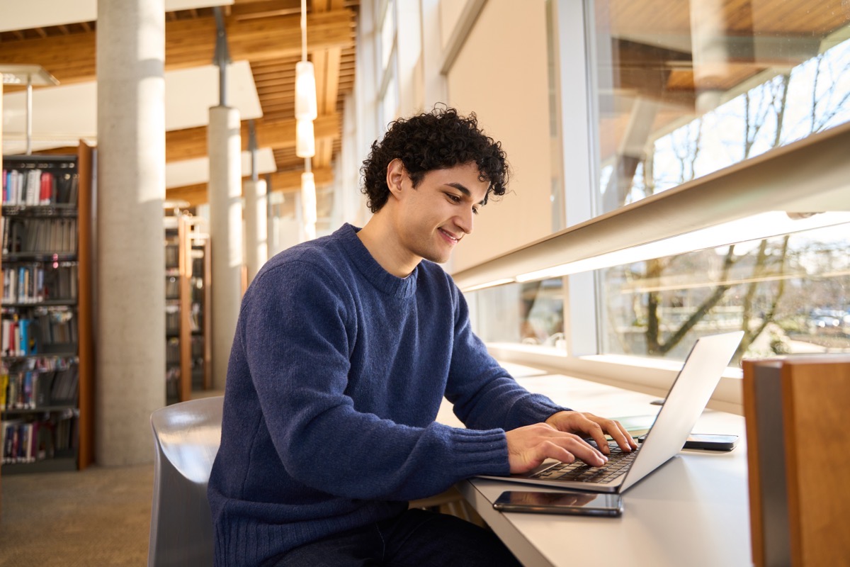 A student working independently on a laptop in a school library, smiling.